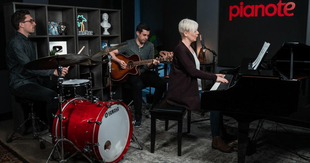 Becoming a multi-instrumentalist can help you join a band. Band in Pianote studio including drummer, acoustic guitarist, and Lisa playing piano and singing.