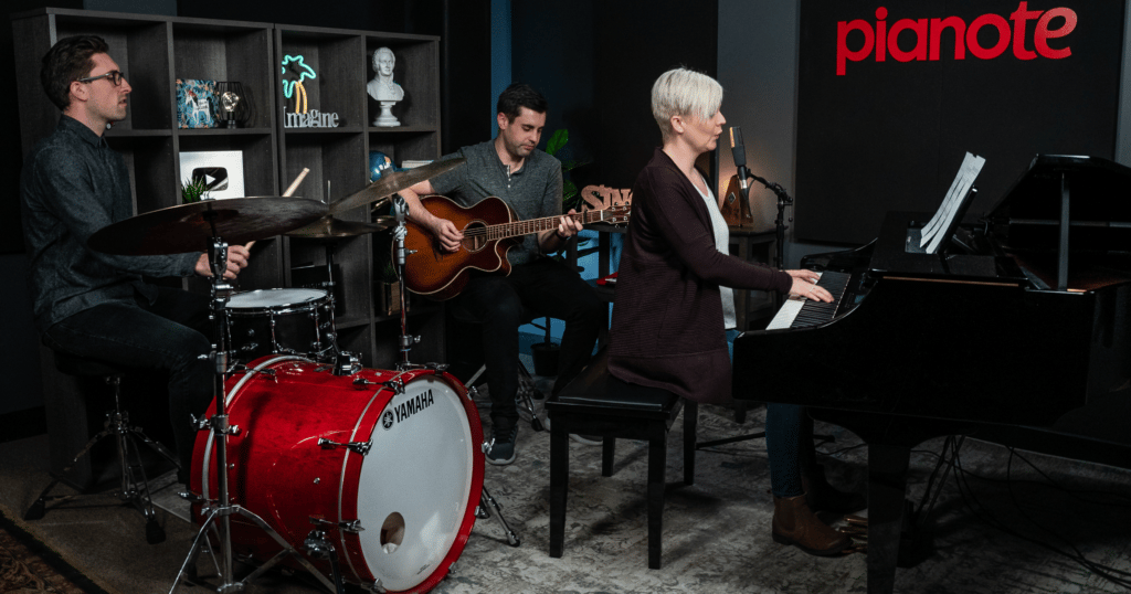 Becoming a multi-instrumentalist can help you join a band. Band in Pianote studio including drummer, acoustic guitarist, and Lisa playing piano and singing.