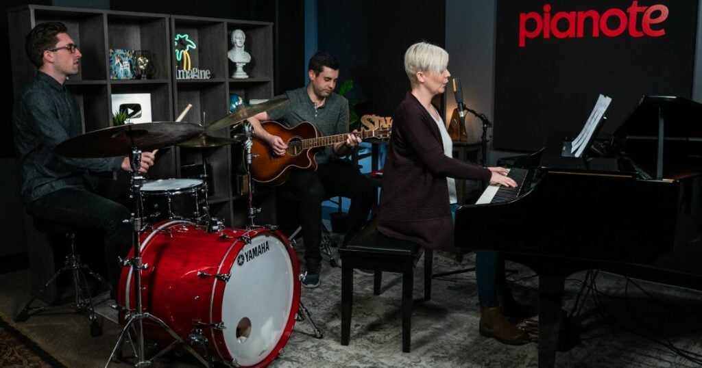 Screenshot of 10 Easy Piano Songs -Lisa as pianist with guitarist and drummer playing together in Pianote studio.