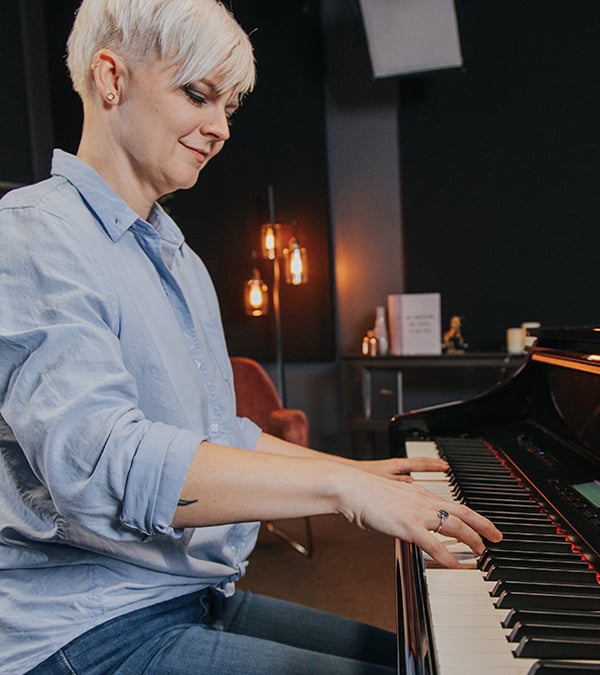 Woman with shrot platinum hair and blue blouse playing piano, side view.