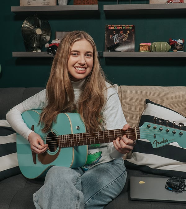 Woman with long dark blonde hair playing turquoise acoustic guitar.