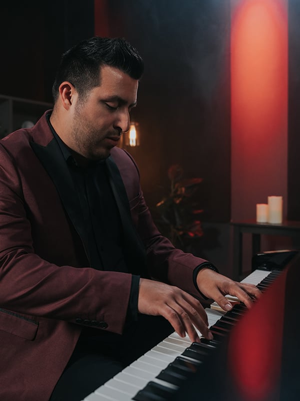 Man with black hair in burgundy suit playing piano.