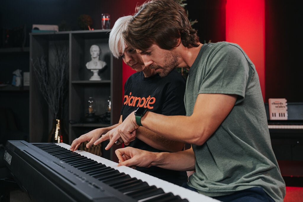 Woman with platinum short hair in black tshirt and man with brown hair and green tshirt playing and pointing at keys.