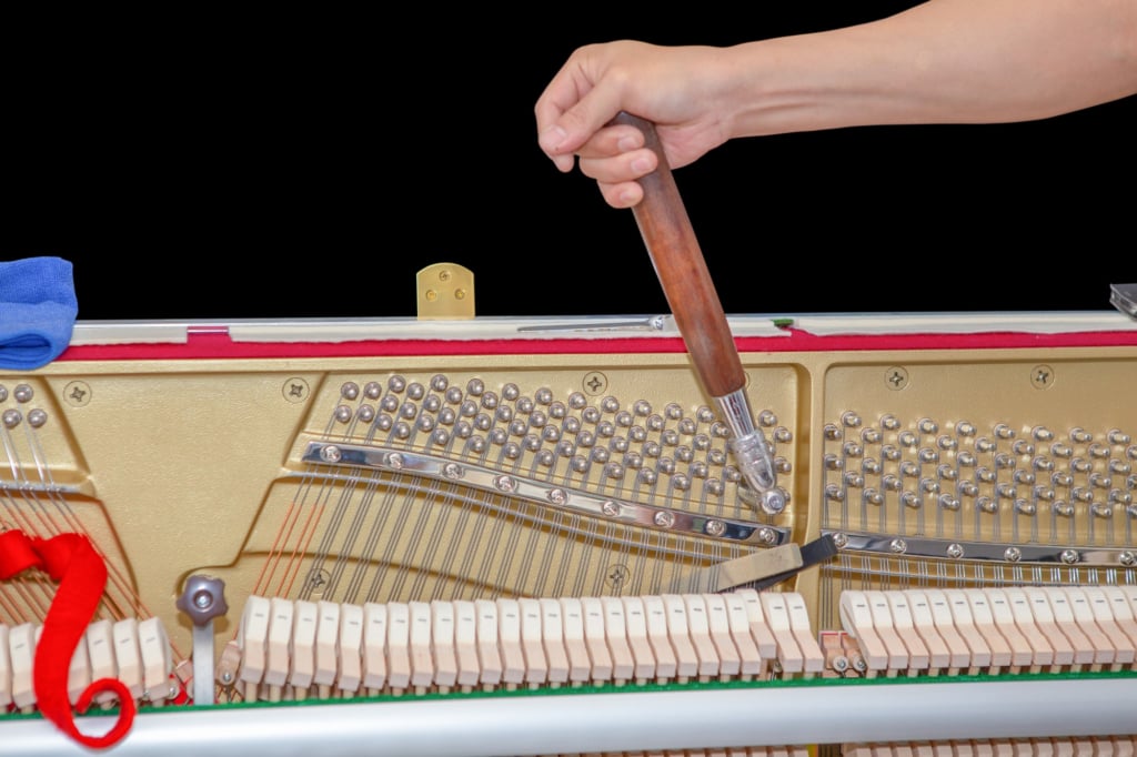 Arm turning pinblock on exposed upright piano with tuner.