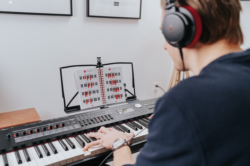 Music theory basics. Man with headphones playing keyboard with book of chords on music stand.