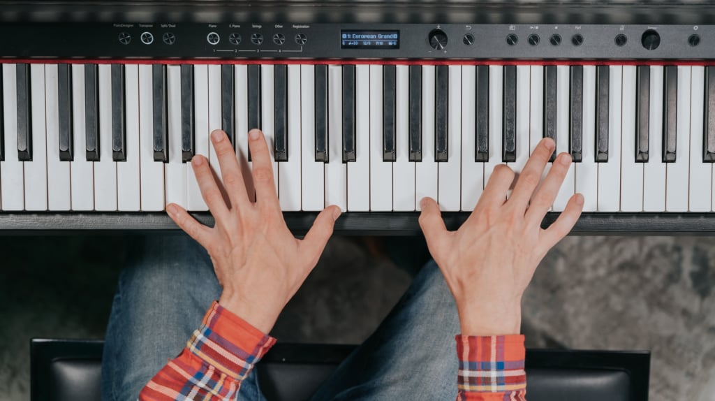 Overview of hands in orange plaid sleeves playing piano.