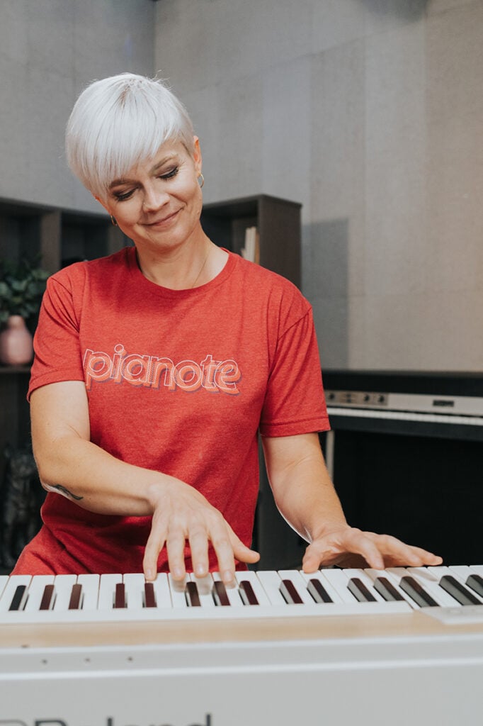 Woman with short platinum hair and red Pianote T-shirt playing white keyboard.