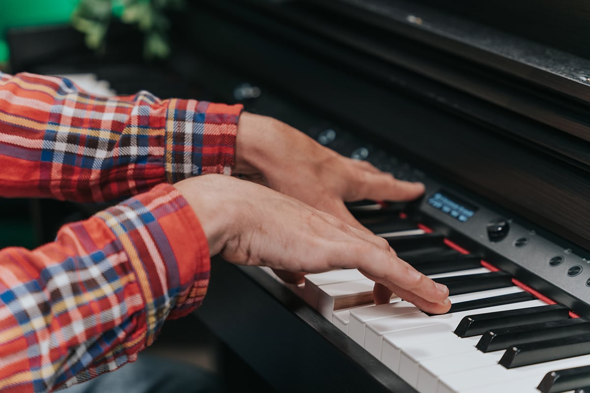 How to learn piano fast. Close up of hands on piano keyboard with red plaid sleeves.