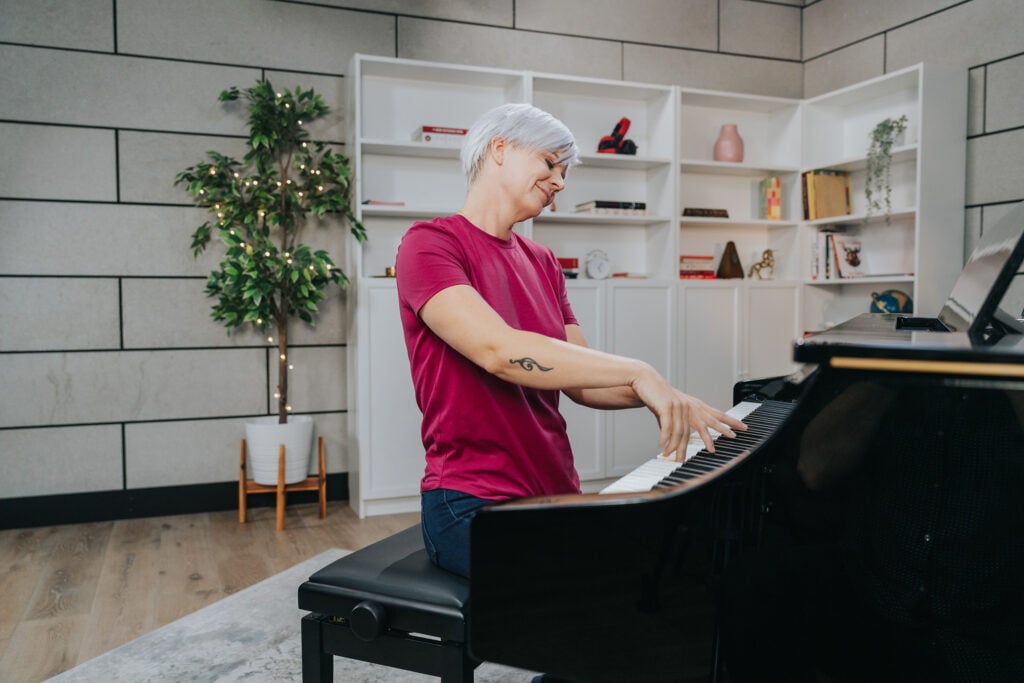 Woman in dark pink shirt with short platinum hair playing piano dramatically.