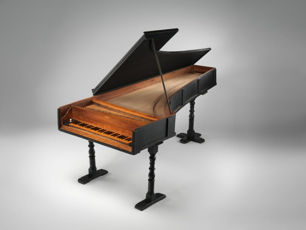 Who invented the piano? Grand piano by Bartolomeo Cristofori: a smaller, black, piano-shaped instrument in a white museum background.