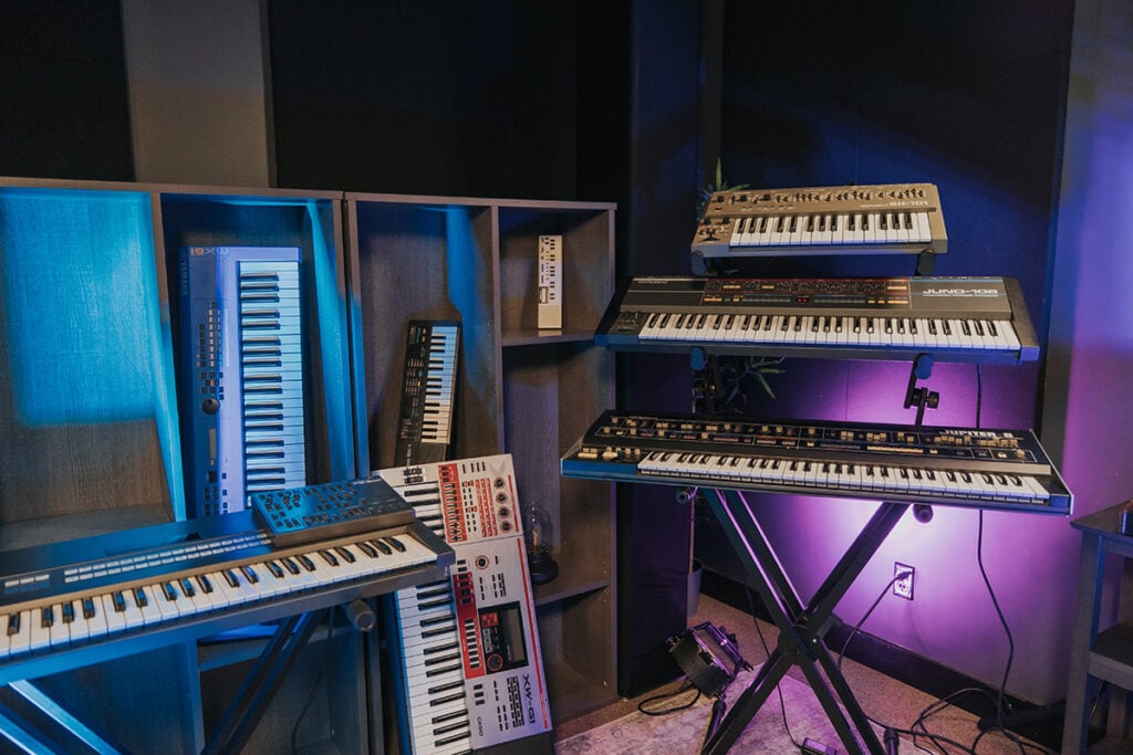 Synth keyboards in purple and blue lit studio.