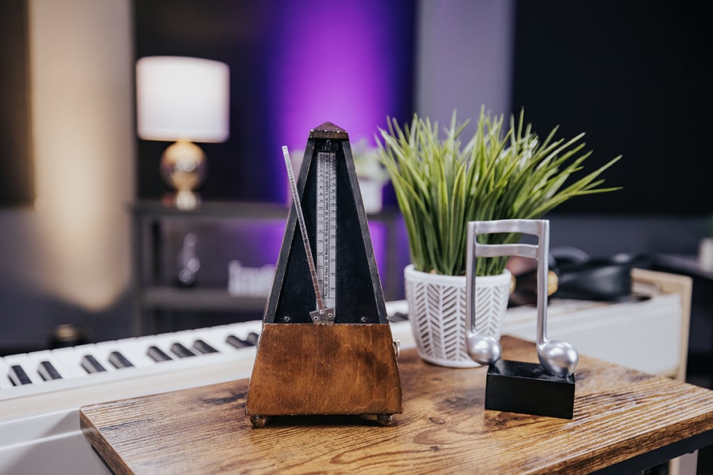 Triangular metronome on side table next to sixteenth note sculpture in front of white keyboard in purple lit studio.