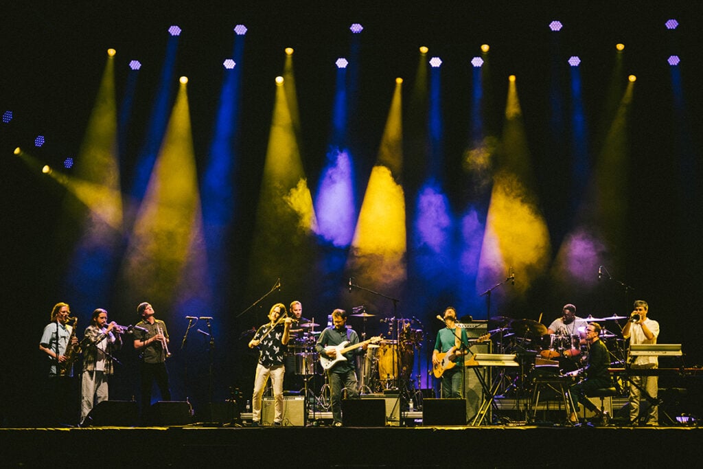 Large band playing instruments on stage with blue and yellow strobe lights.