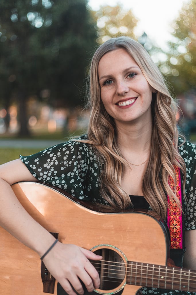 Woman with long blonde hair sitting with guitar.