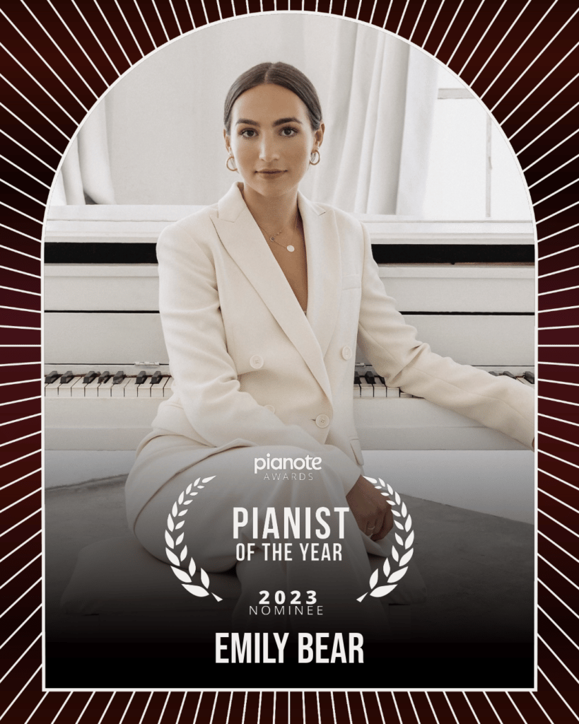 Emily Bear. Young woman in white pantsuit sitting in front of white piano.