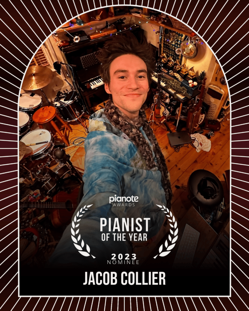 Jacob Collier. Man in blue tie-dye taking selfie in front of home studio filled with music instruments.
