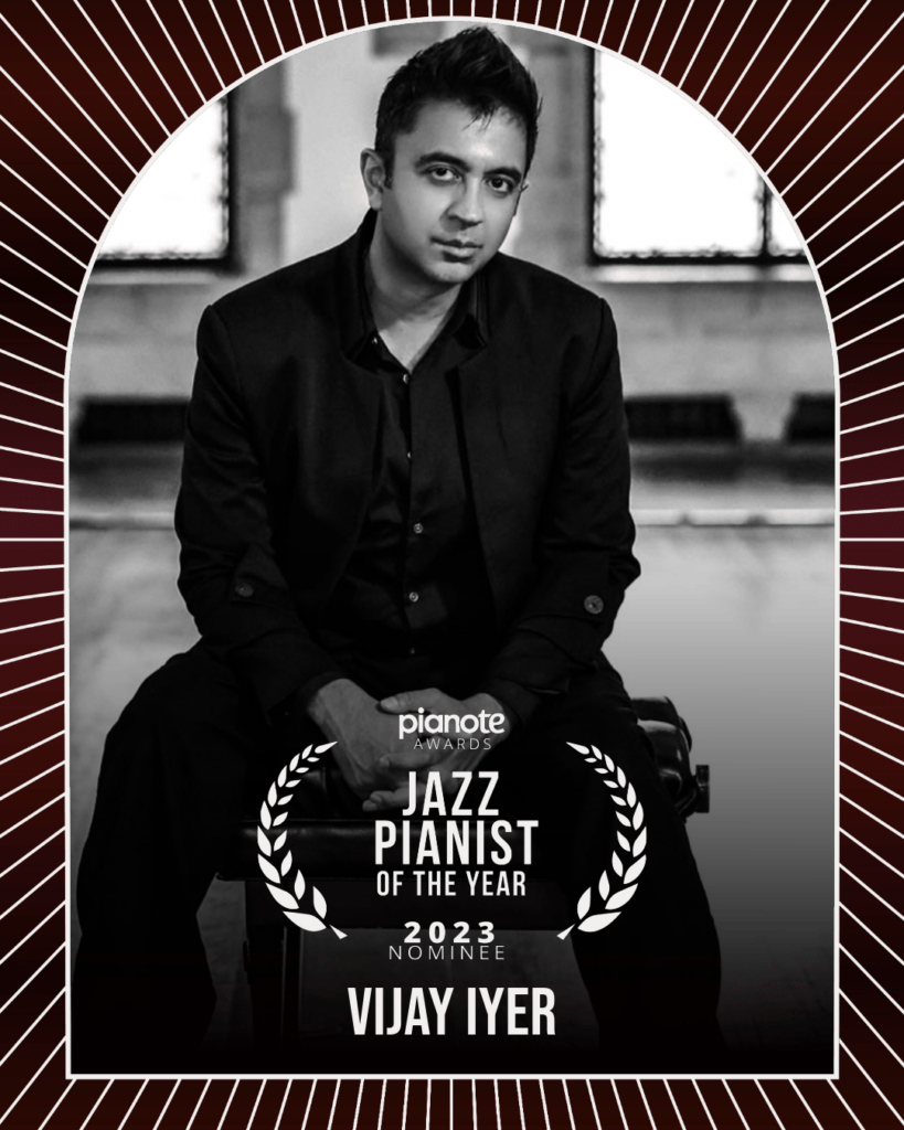 Vijay Iyer. Black and white photo of man sitting in a wide open studio.