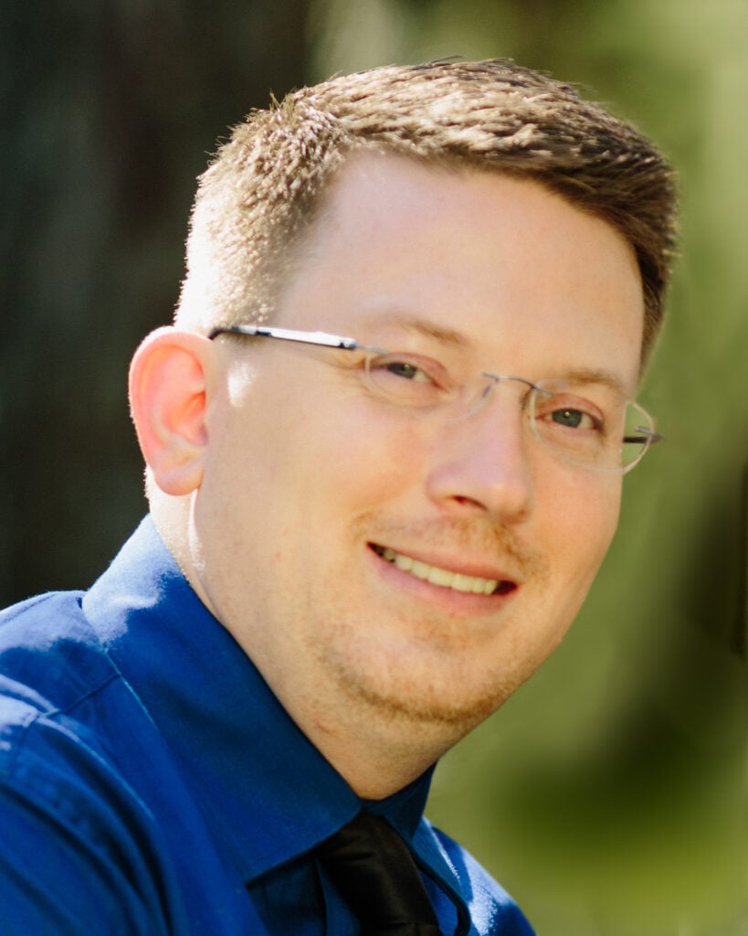 Portrait of a man with glasses in blue collared shirt.