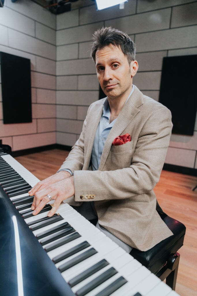 Man in khaki suit jacket with red pocket square playing piano. How to play ragtime piano.