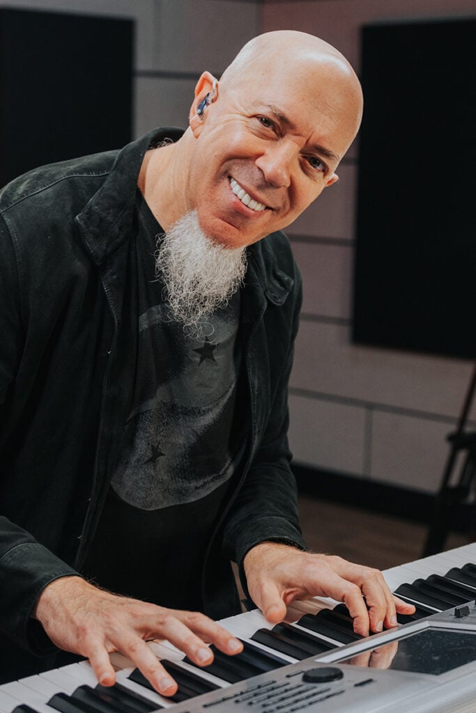 Man with goatee smiling and looking up from playing on a silver keyboard.