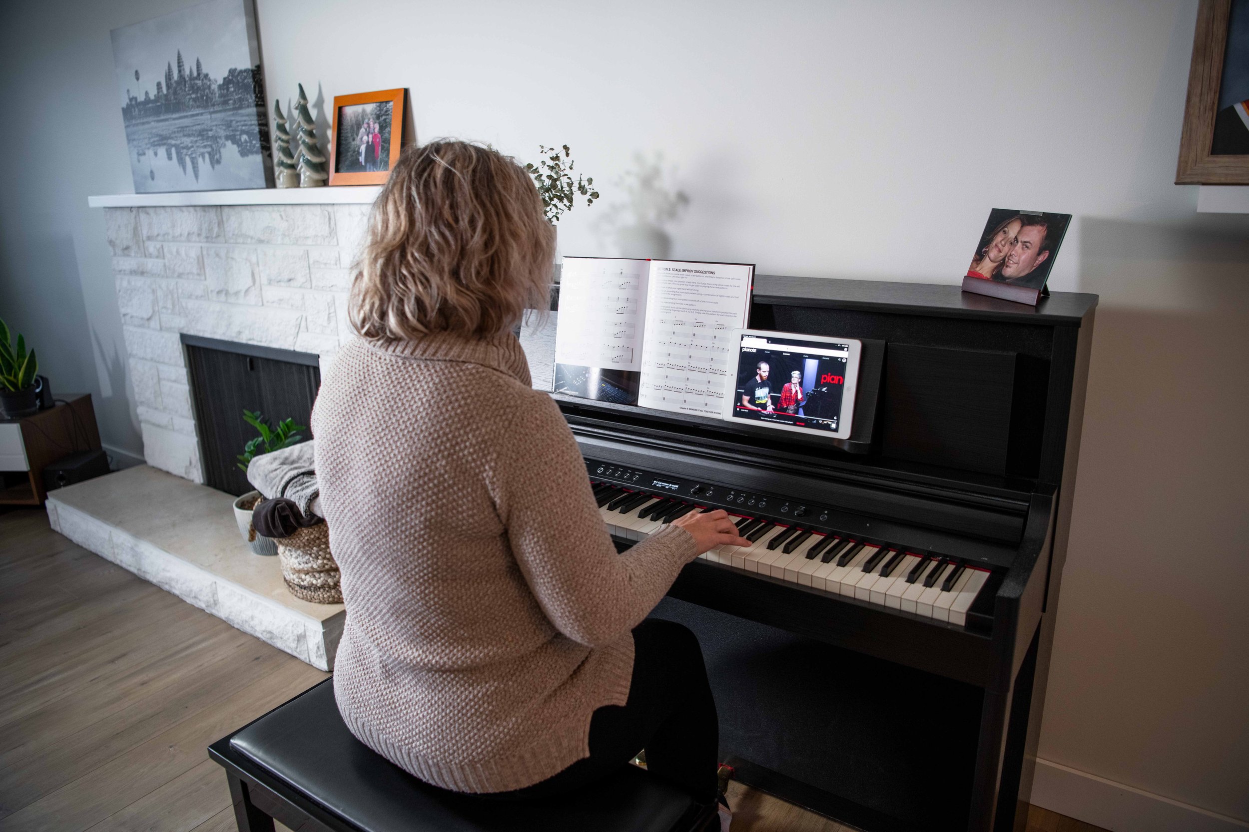 Woman playing console keyboard (upright piano) at home with book and iPad.