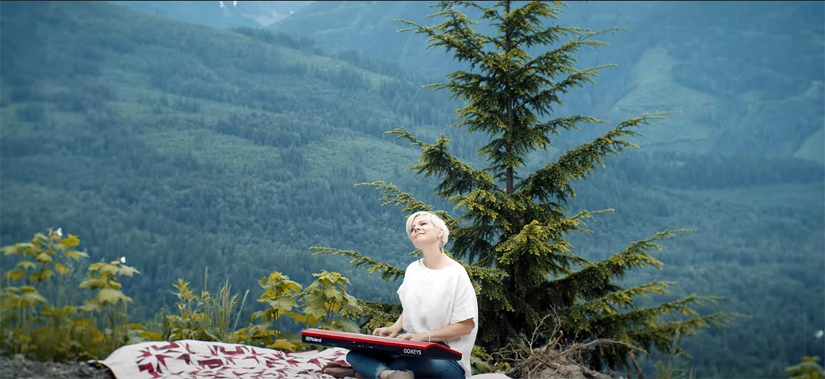 Lisa sitting on picnic blanket with keyboard on lap in front of a mountain background.