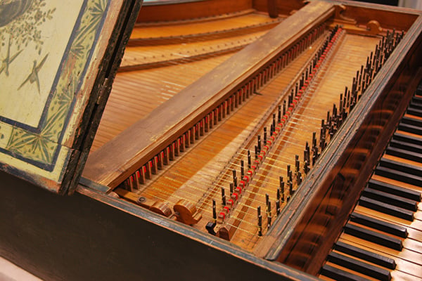 Old, intricate wooden keyboard instrument with lid open showing strings.