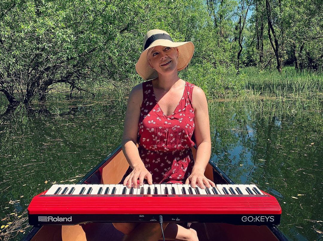 Lisa playing red Roland GO:KEYS while sitting in a canoe in the water.