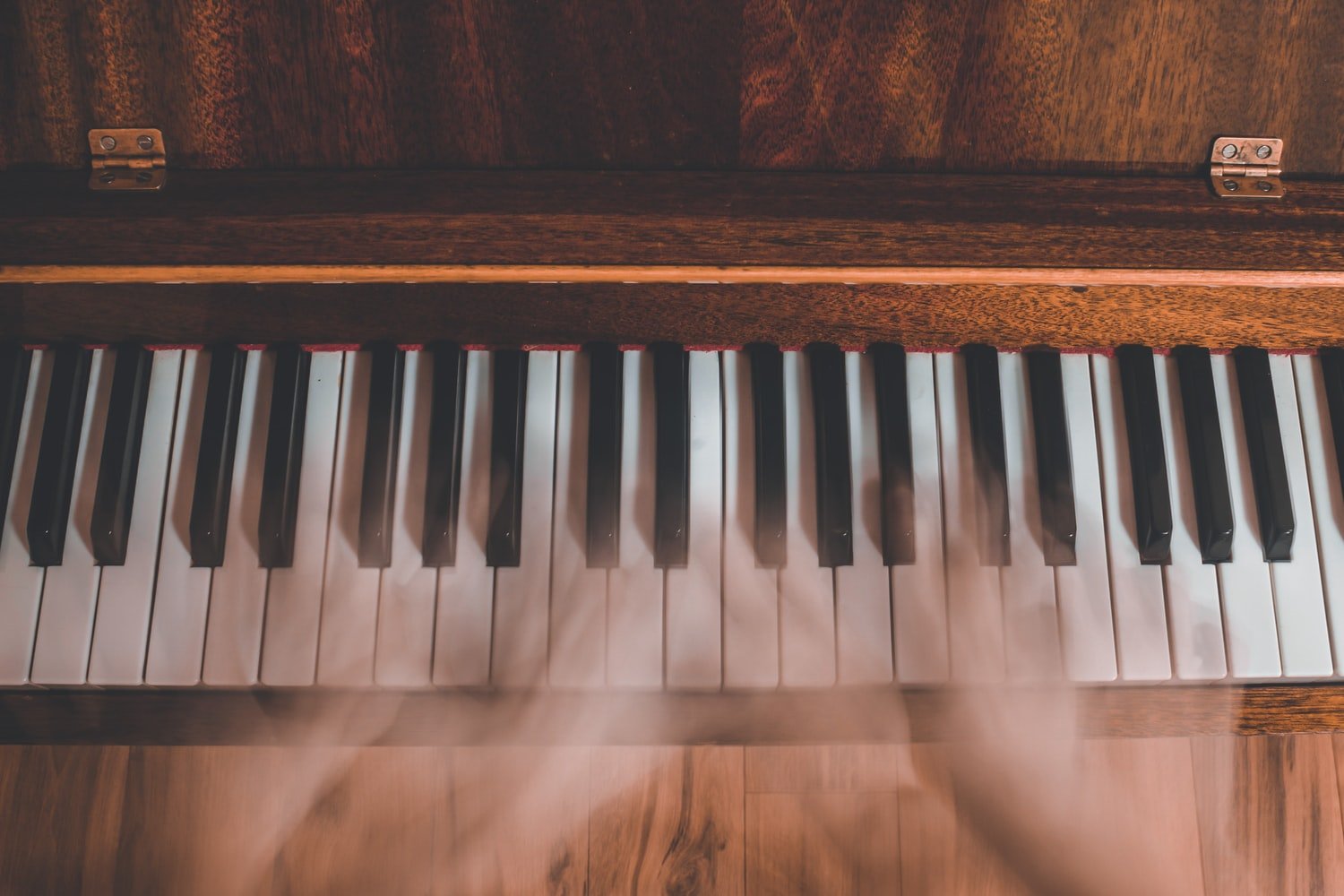Bird's eye view of piano keyboard in wood finish with blurry hands.