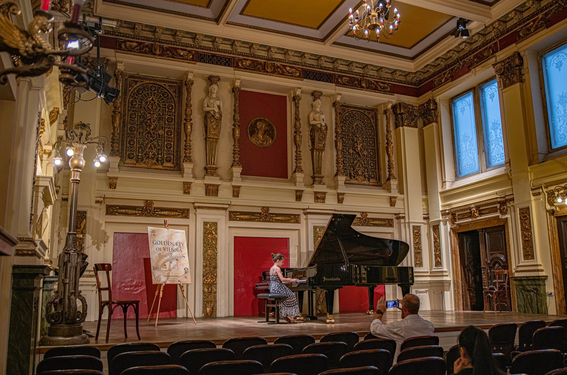 Woman plays grand piano in ornate old gold gilded room.