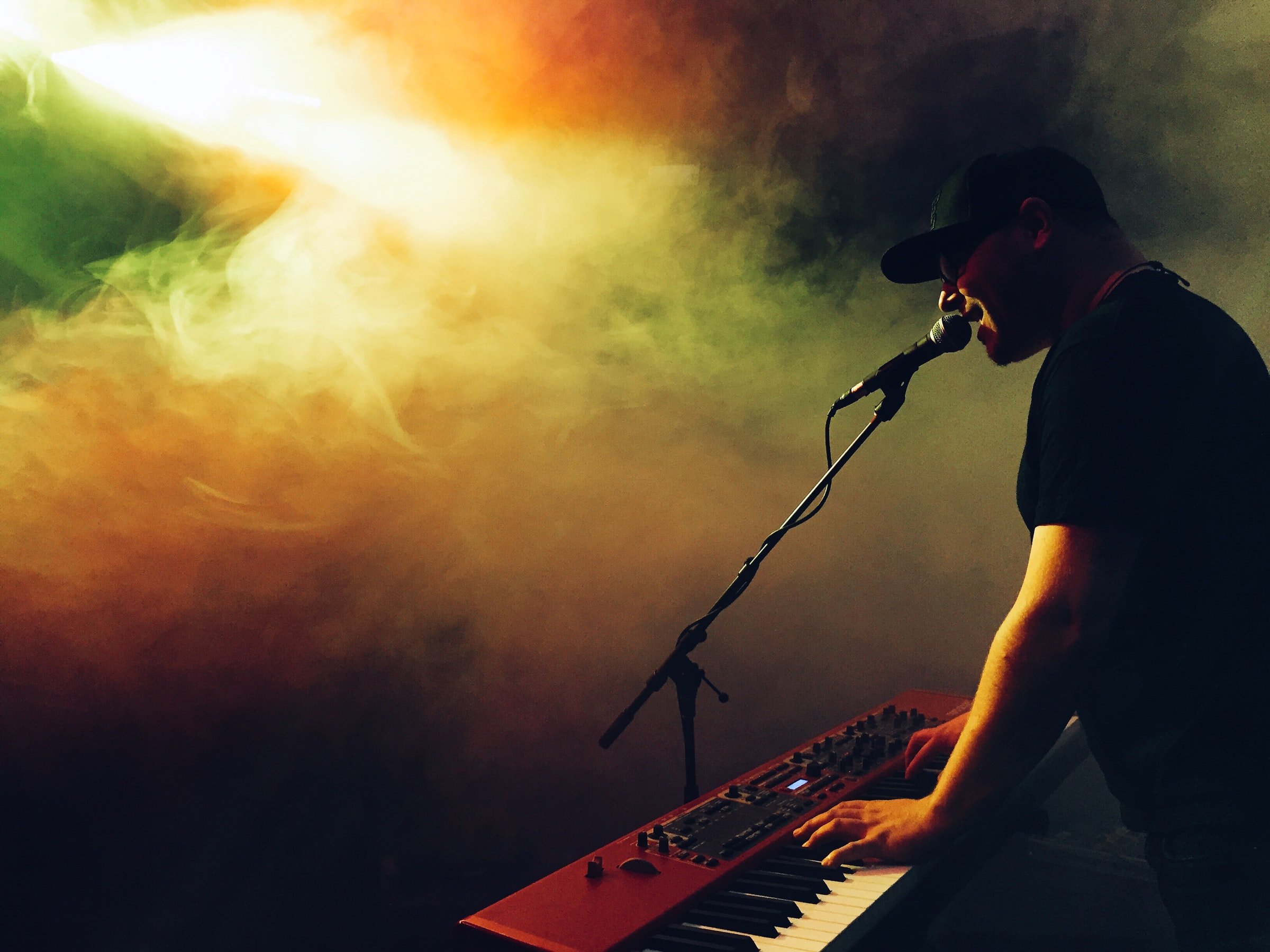Man playing keyboard and singing in colorful smoke.