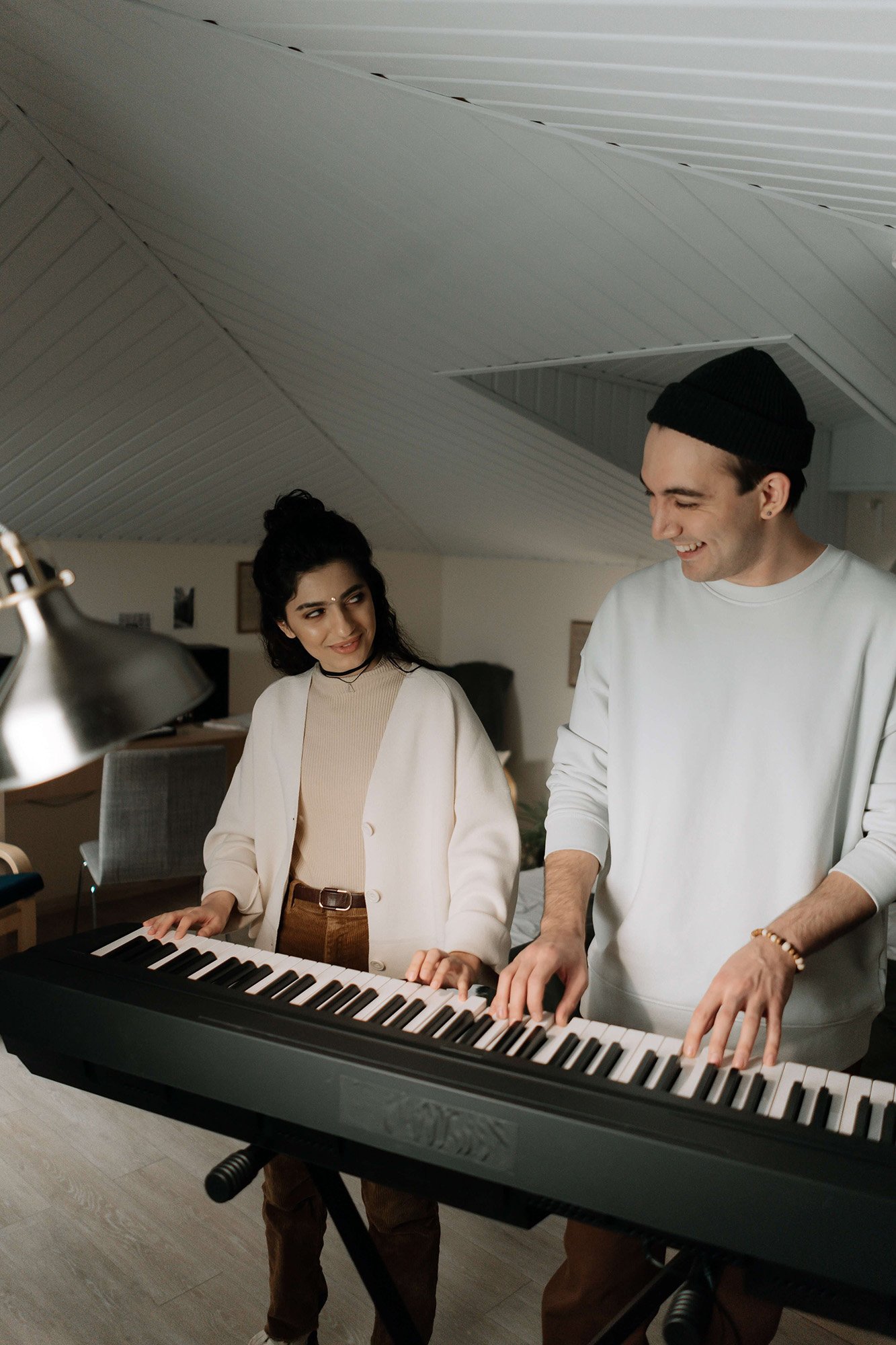 Man and woman playing keyboard together in low ceiling room.