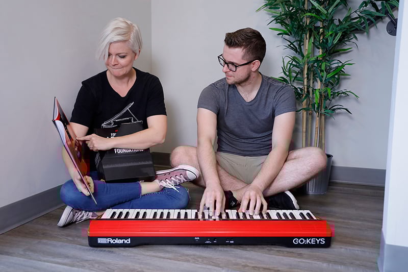 Lisa and Sam sitting on the ground looking at books and playing on red keyboard.