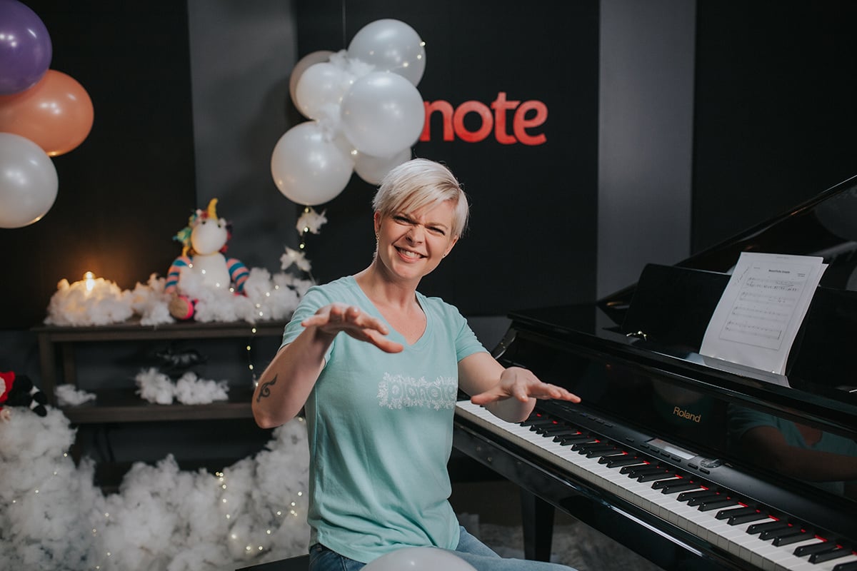 Lisa at piano holding up hands against background set of clouds and unicorn and fairylights.