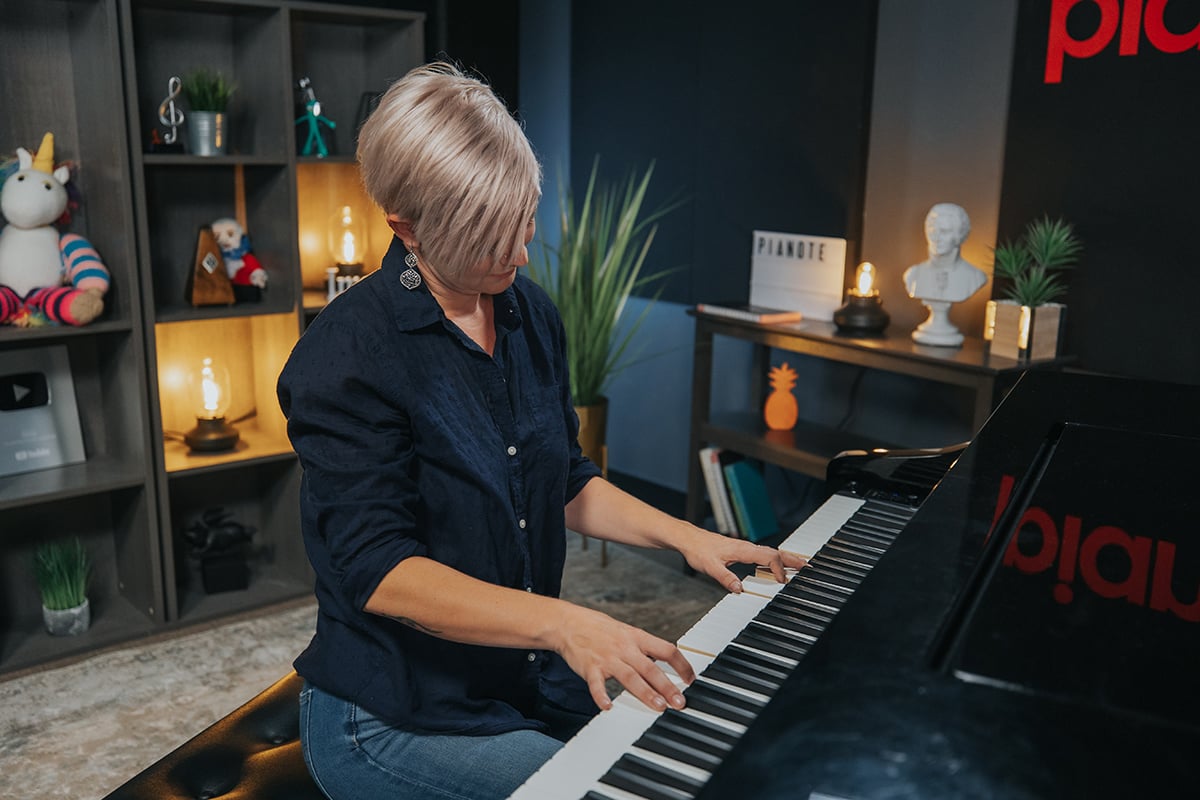 Lisa playing piano, hair angled towards camera. Unicorn stuffy in shelf in background.