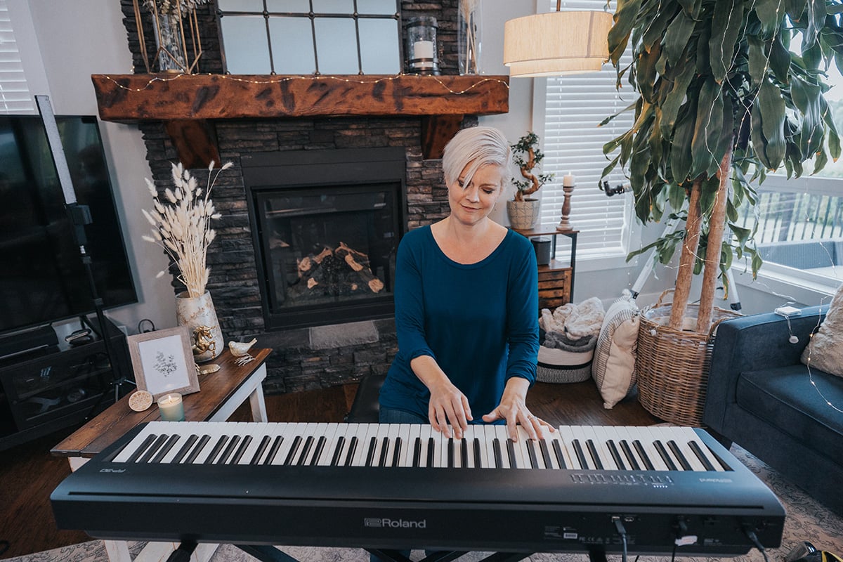 Lisa playing keyboard in living room decorated with plants in front of a fireplace.