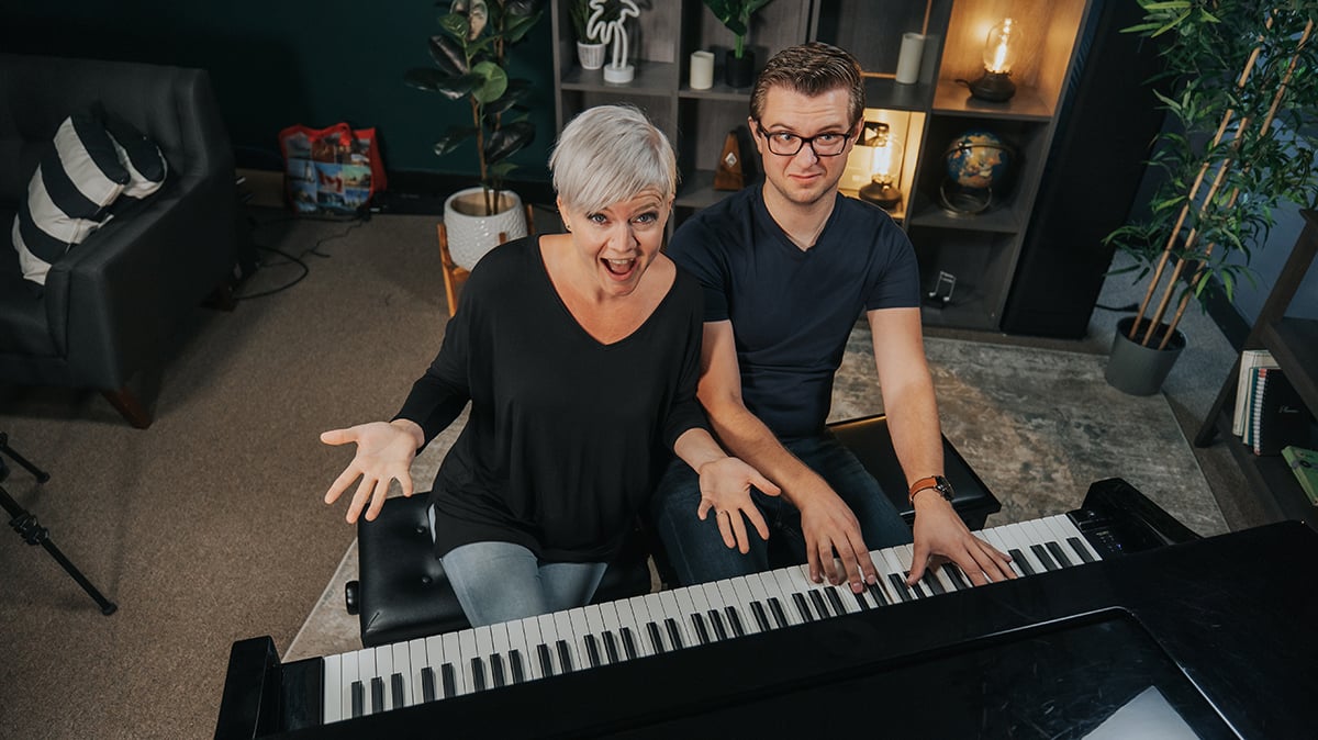 Lisa and Sam on the piano. Sam is playing with a twisted up face. Lisa has hands and mouth open like "hey."