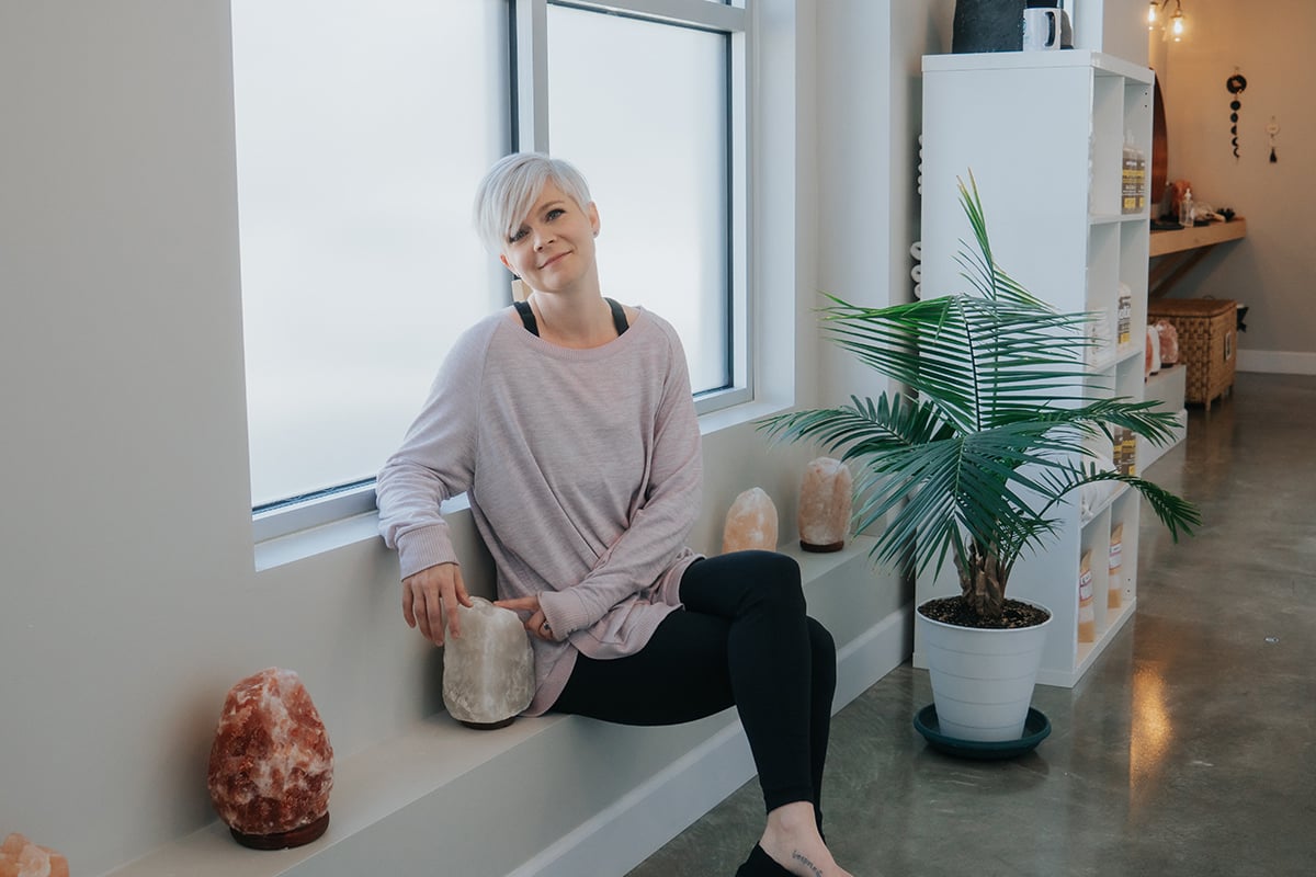 Lisa in clean white room sitting on ledge with crystals.