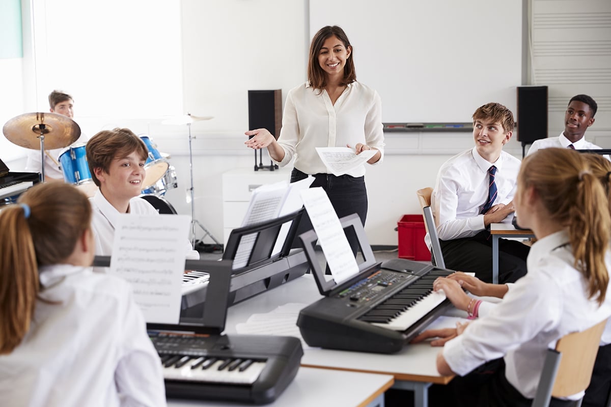 Students playing keyboards in a classroom with female teacher.