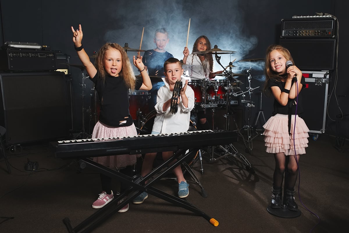 Young children posing with band instruments (keyboard, mic, drum set and amps).