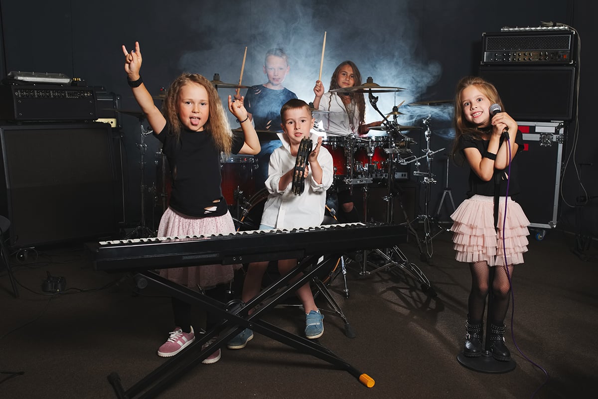 Young children posing with band instruments (keyboard, mic, drum set and amps).