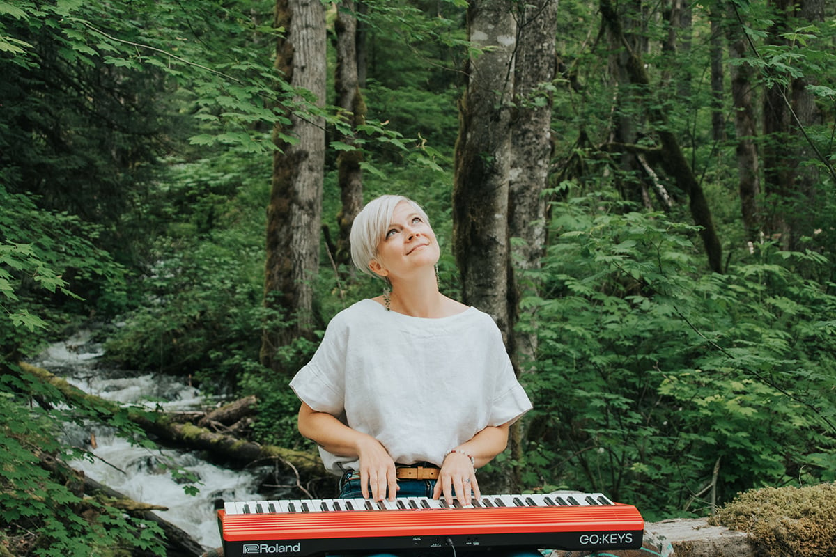 Benefits of playing piano. Woman with short platinum hair playing red keyboard in front of a brook in a forest.