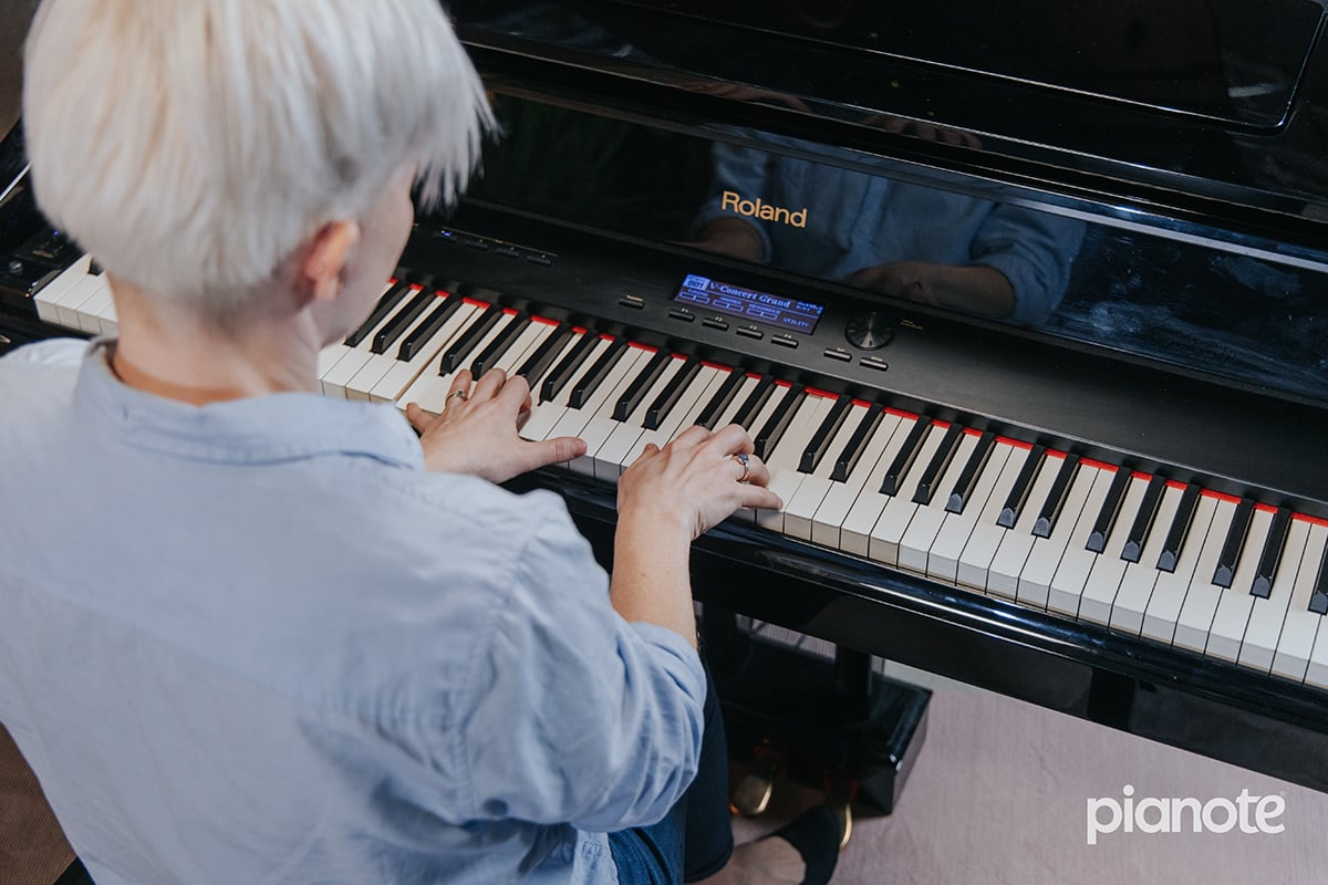 Piano practice motivation: shot from behind above of woman in blue blouse and platinum hair playing piano.