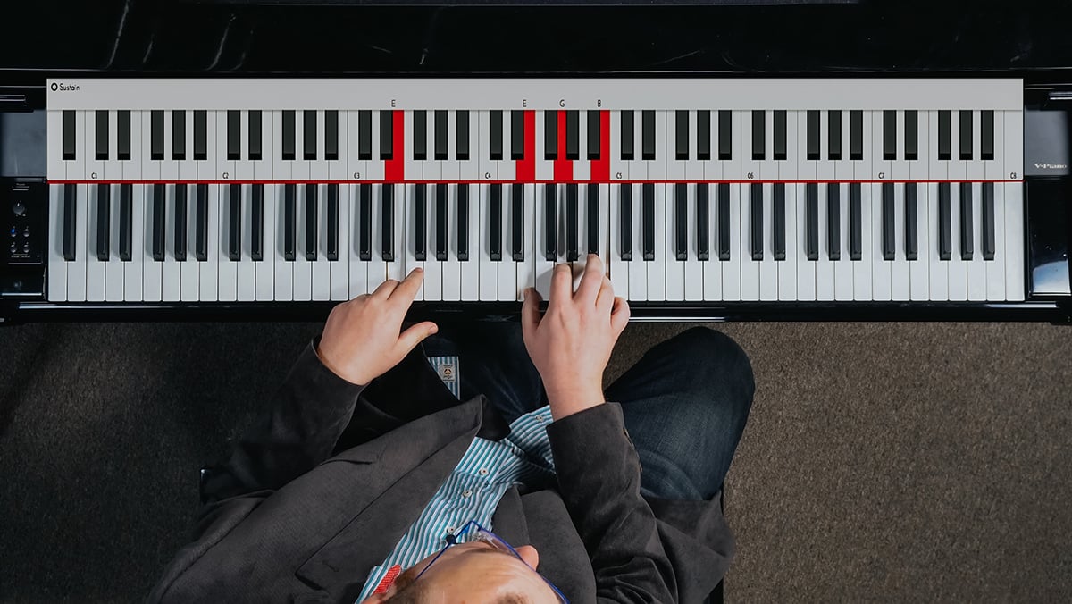 Bird's eye view of man in suit's hands playing piano with keys highlighted.