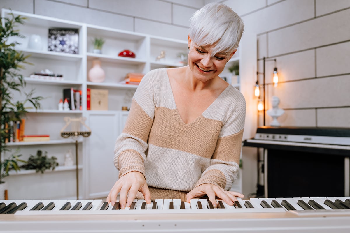 Woman with short platinum hair in beige striped sweater playing oak colored piano in light studio.