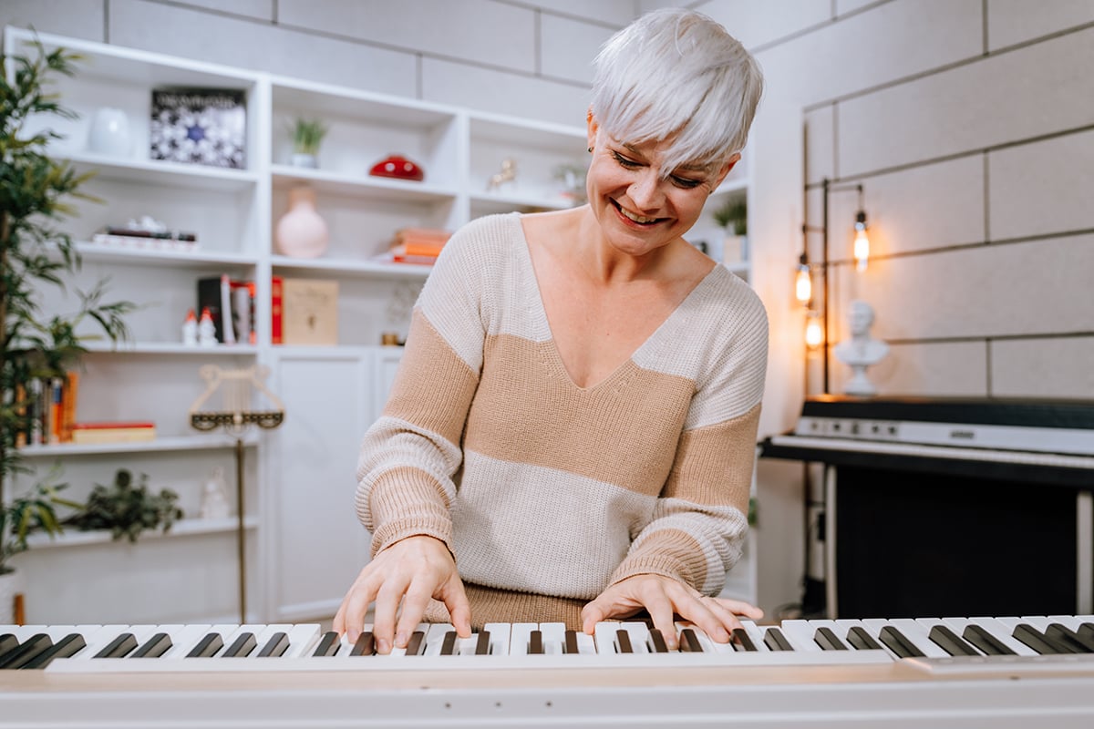 Woman with short platinum hair in light stripey sweater playing keyboard.